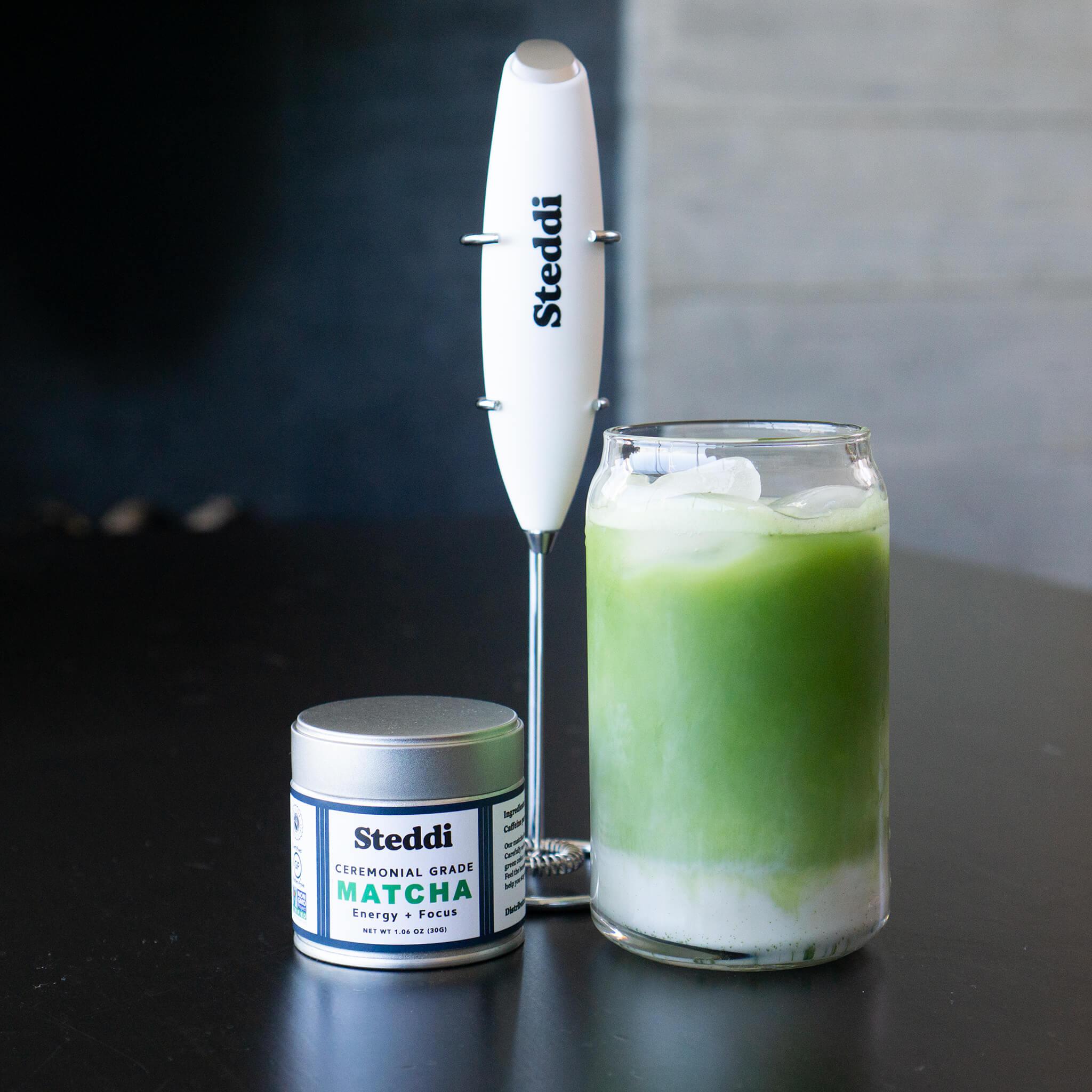 Matcha latte with a milk frother and a matcha tin.